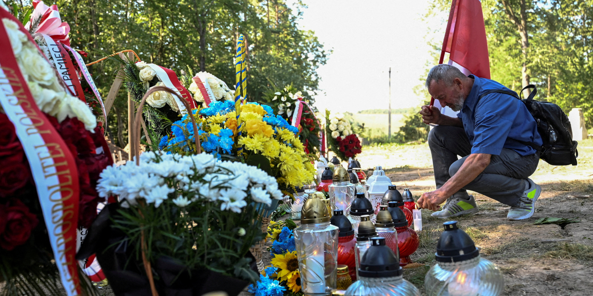 Чоловік тримає польський прапор і запалює лампадку на місці вшануання жертв Волинської трагедії у&nbsp;селі Пужники, Тернопільська область, 6 вересня 2025 (Фото: REUTERS/Anastasiia Smolienko/File Photo)